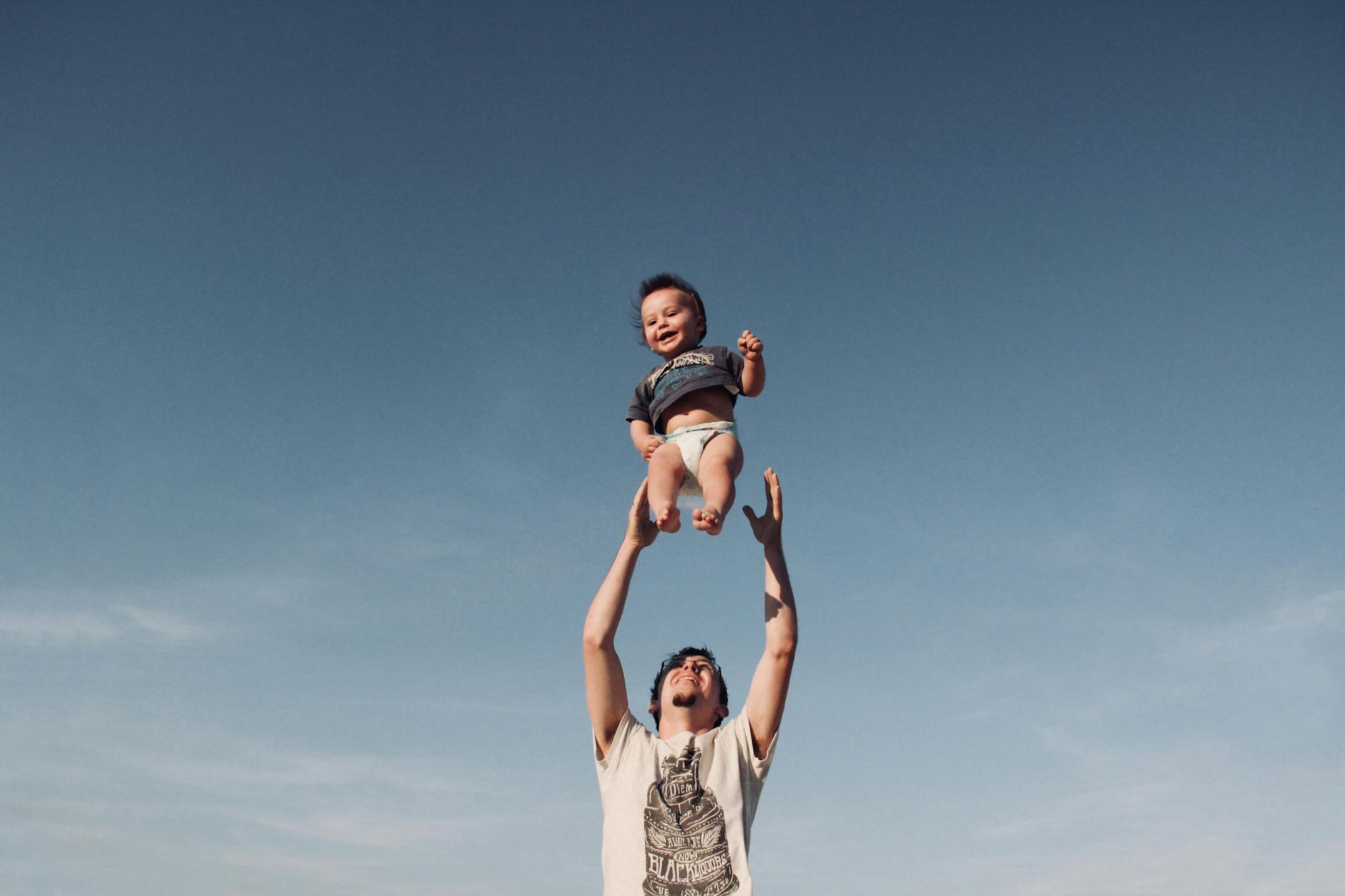photo of a man raising baby under blue sky