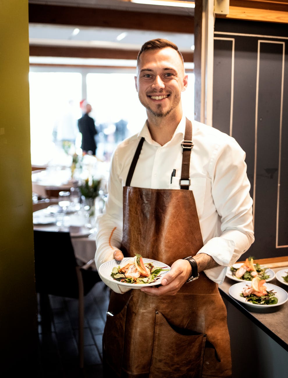 portrait of a waiter in a brown apron holding a dish